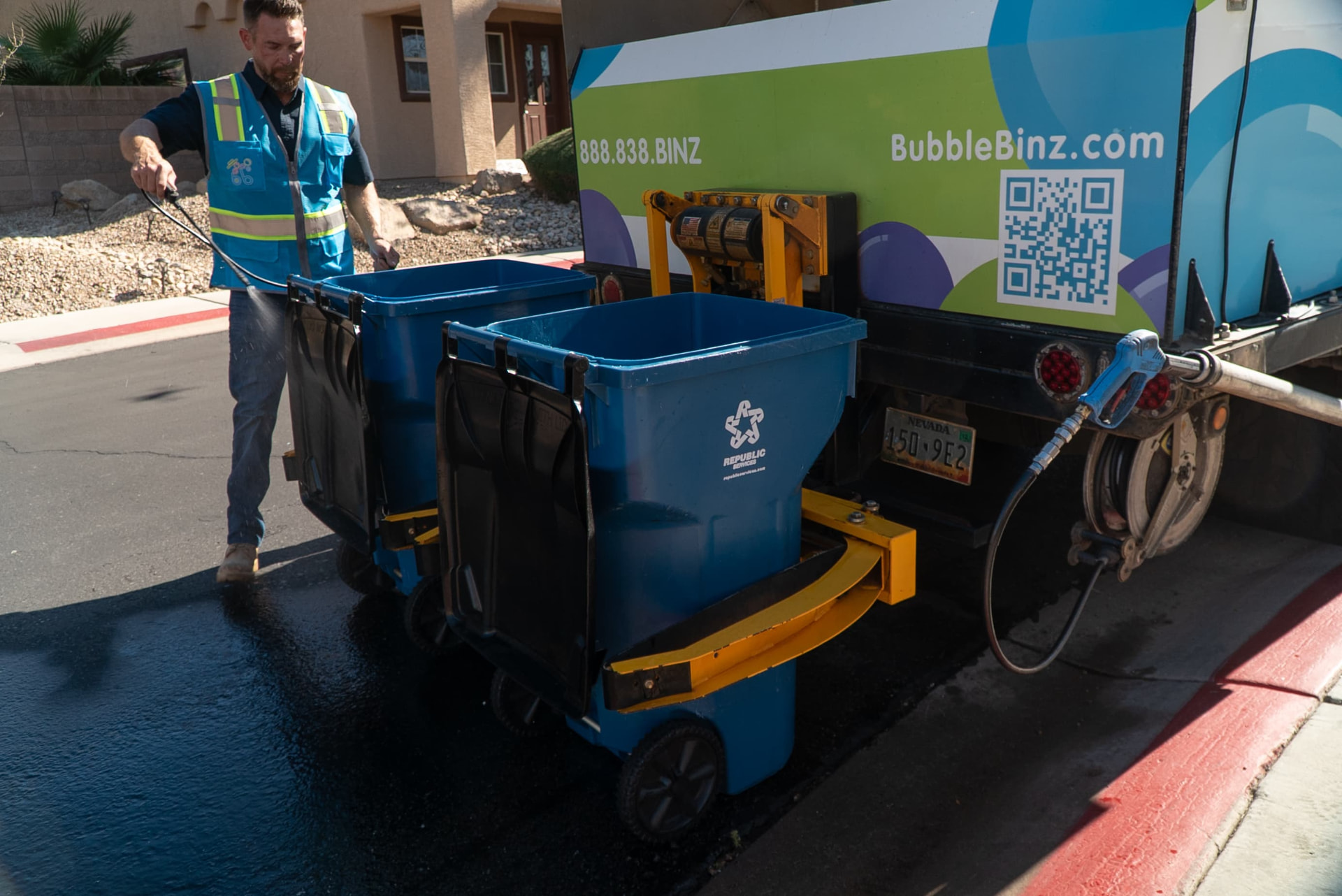 Bubble Binz technician pressure washing curbside trash bins beside a service truck in Las Vegas